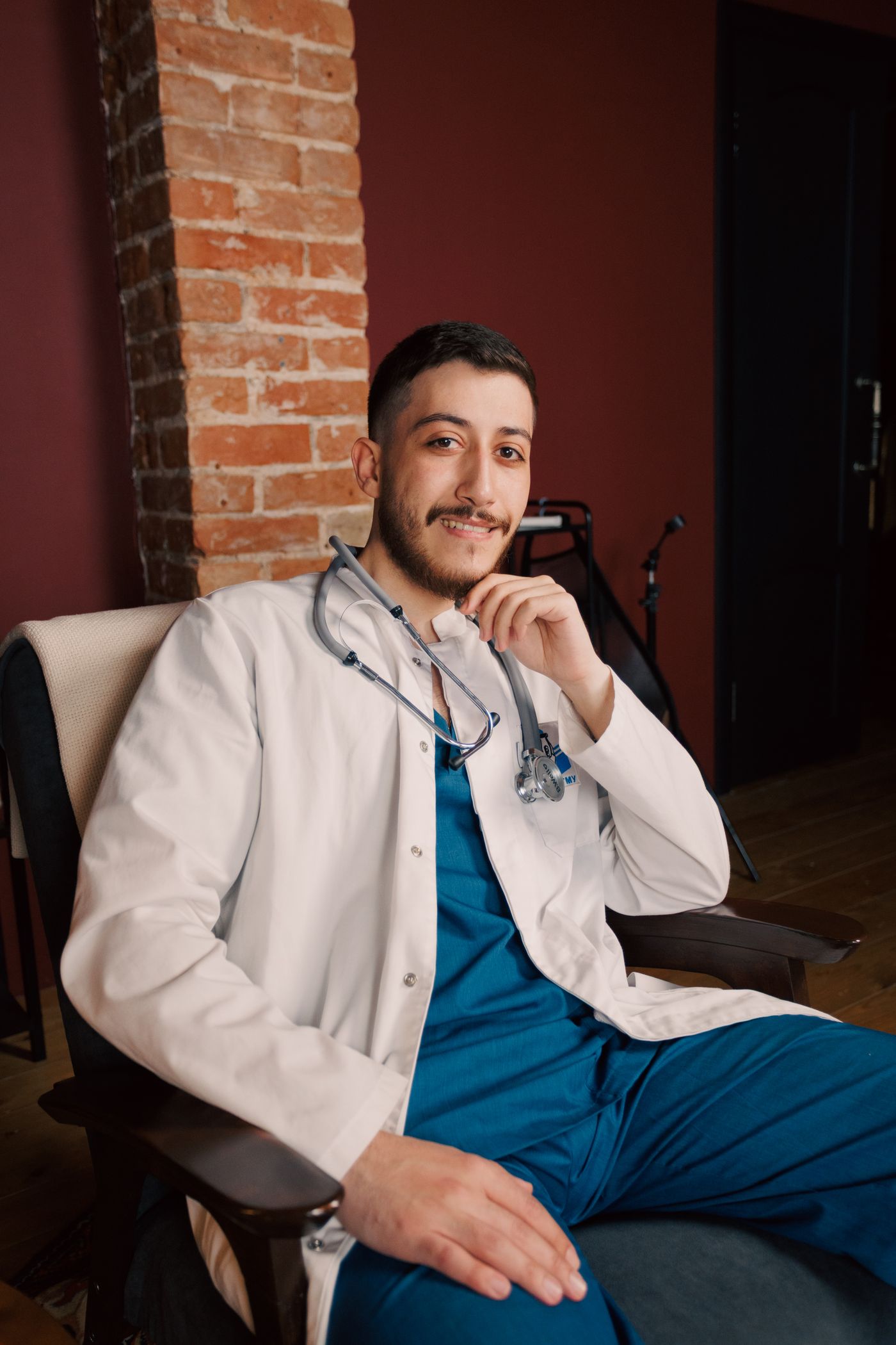 Un médico joven sentado en su consultorio, con bata blanca y estetoscopio